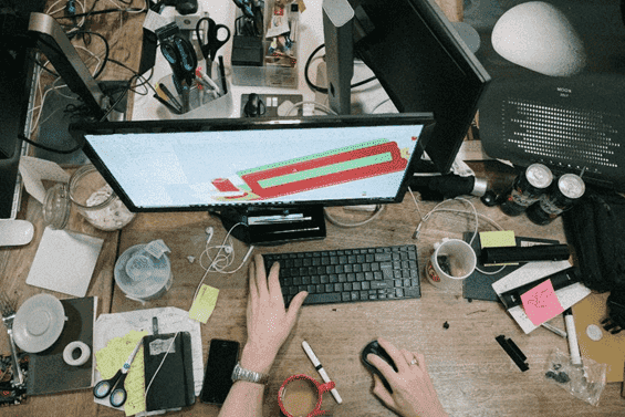 Aerial view of a person typing on a computer surrounded by a messy desk.