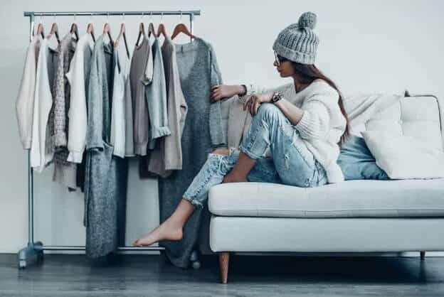 Young woman sitting on a couch and looking at clothes on a rack.