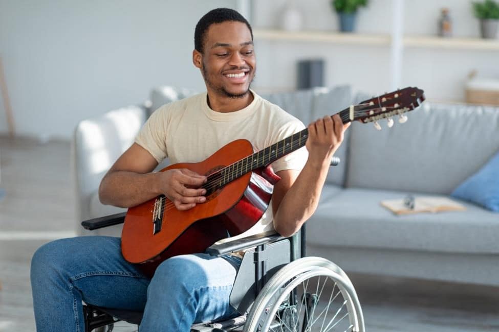 A man playing an acoustic guitar in a wheelchair