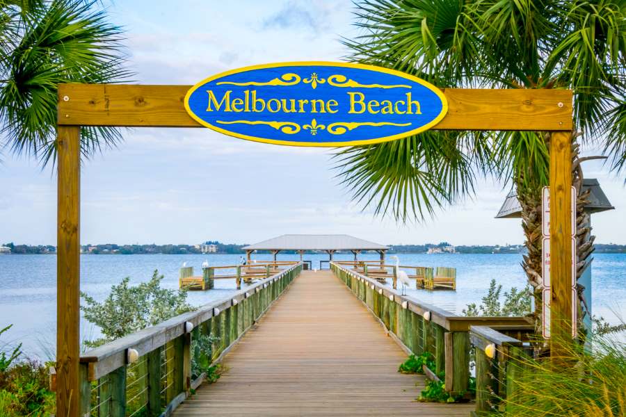 Bright blue and yellow Melbourne beach sign hangs over the beach boardwalk