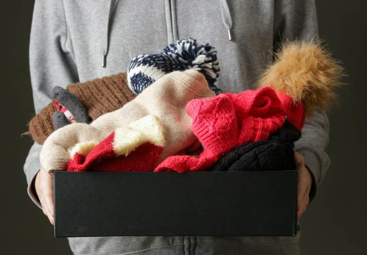 A woman holding a box of gloves and hats for the winter weather.