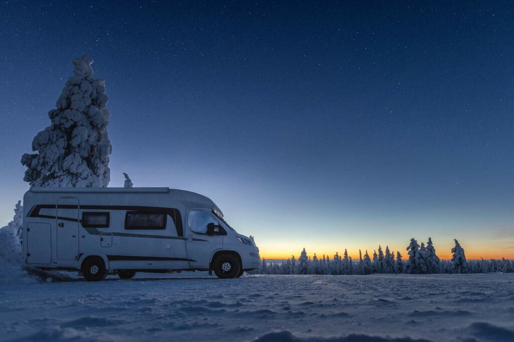 RV parked on a hill in a frozen forest as the sun sets.
