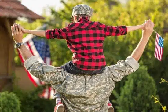 Boy sitting on man's shoulder, holding American flag.